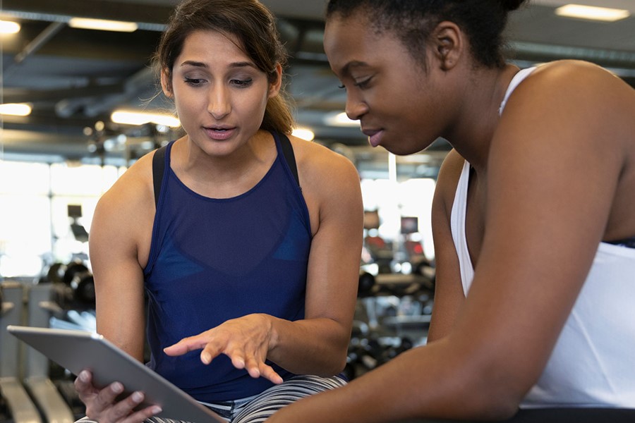 Personal Trainer With Digital Tablet Talking With Woman In Gym