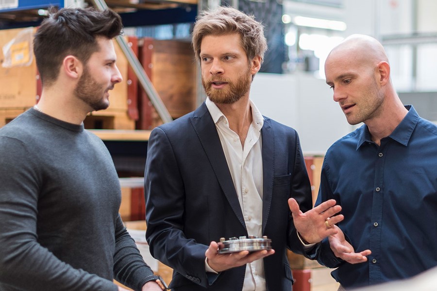 Three Men Talking In Factory Storeroom