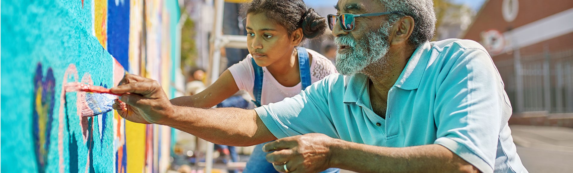 Grandfather And Granddaughter Volunteers Painting Vibrant Mural