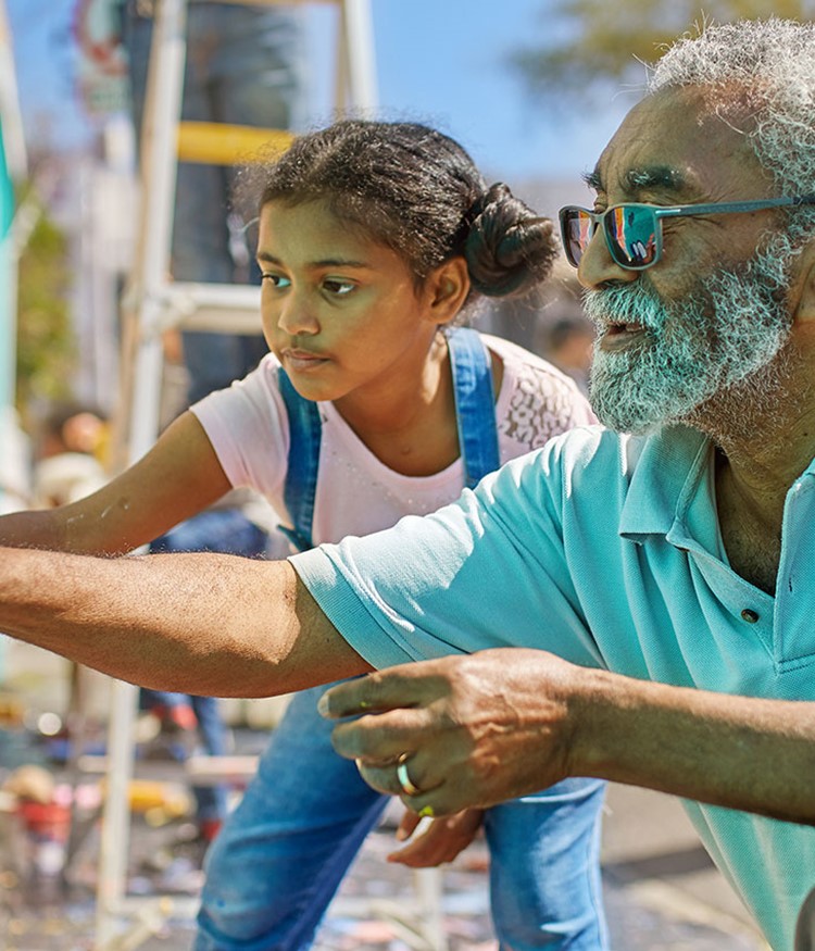 Grandfather And Granddaughter Volunteers Painting Vibrant Mural