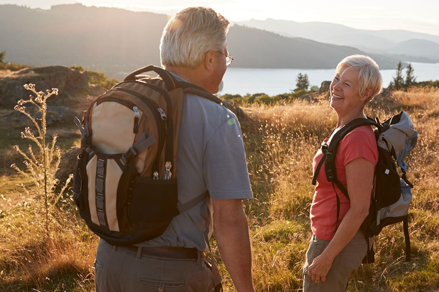 Senior Couple Walking On Top Of Hill On Hike Through Countryside
