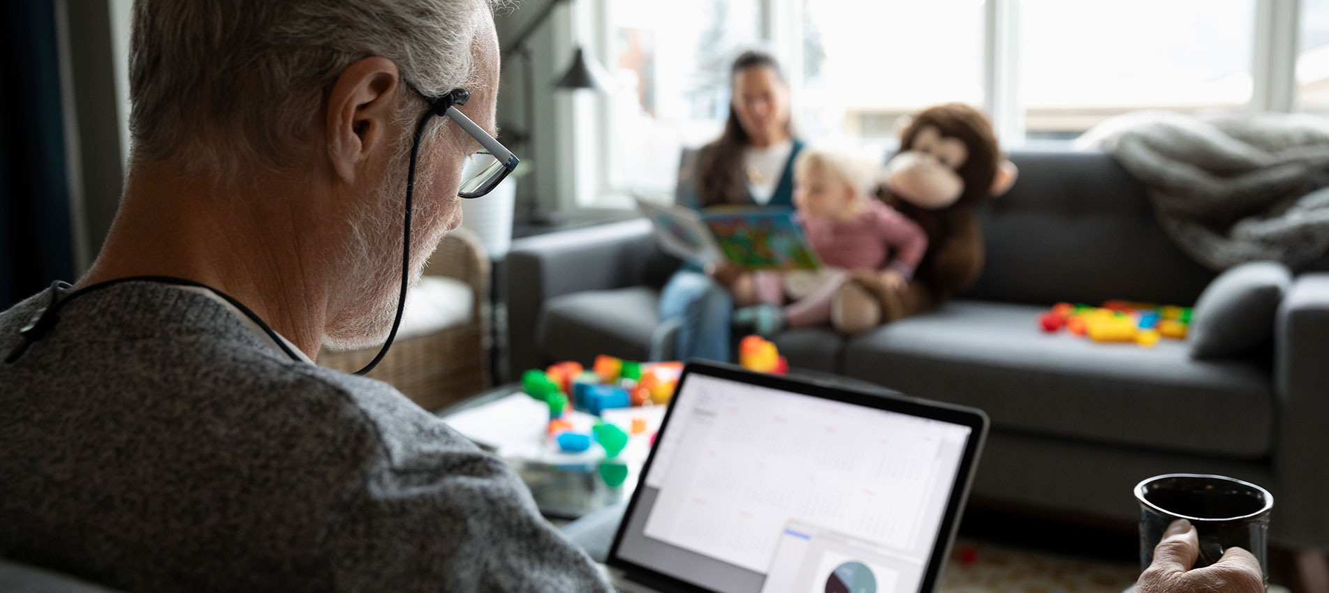 Senior Man Using Laptop And Drinking Coffee In Living Room