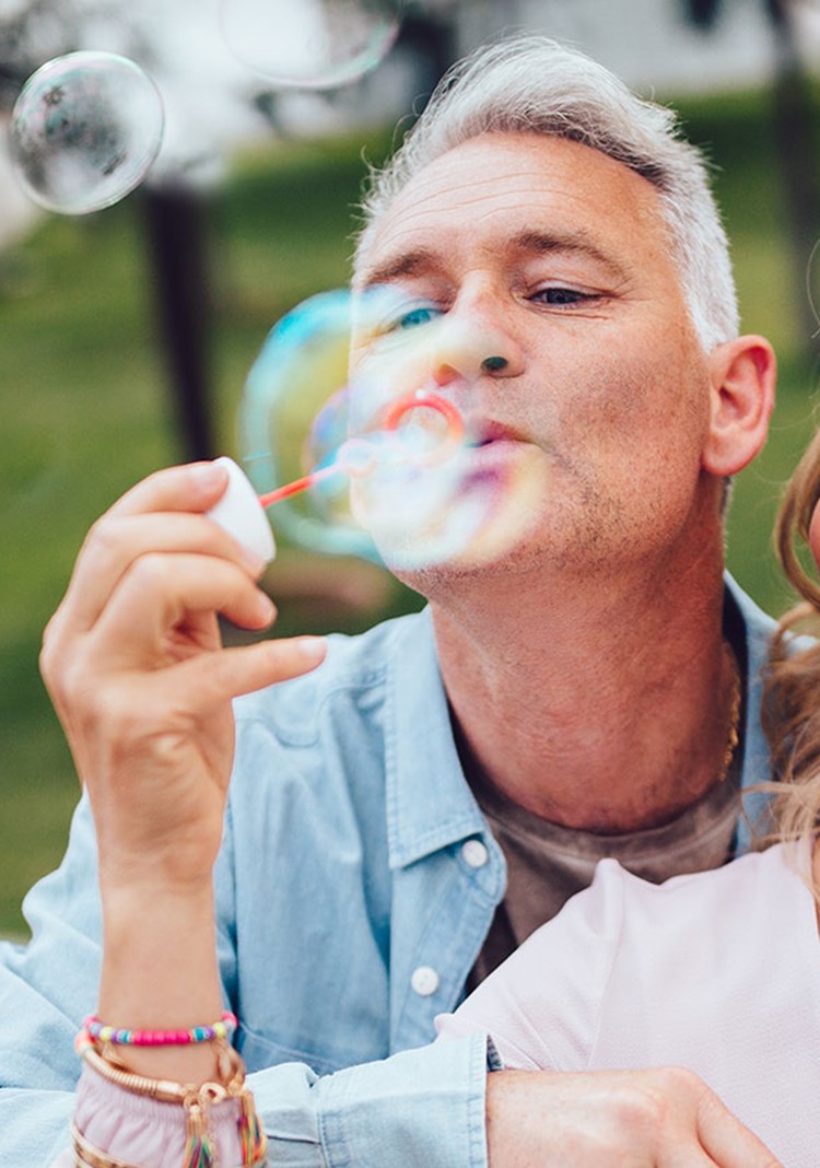 Playful Mature Couple Blowing Bubbles At The Park