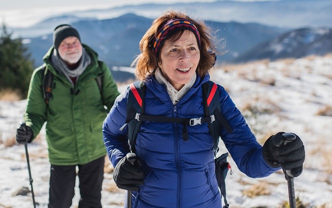 Senior Couple With Nordic Walking Poles Hiking In Snow Covered Winter Nature