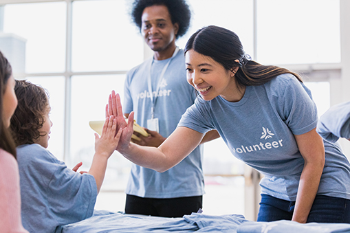 Young Asian Adult Woman High Fives Child Volunteer