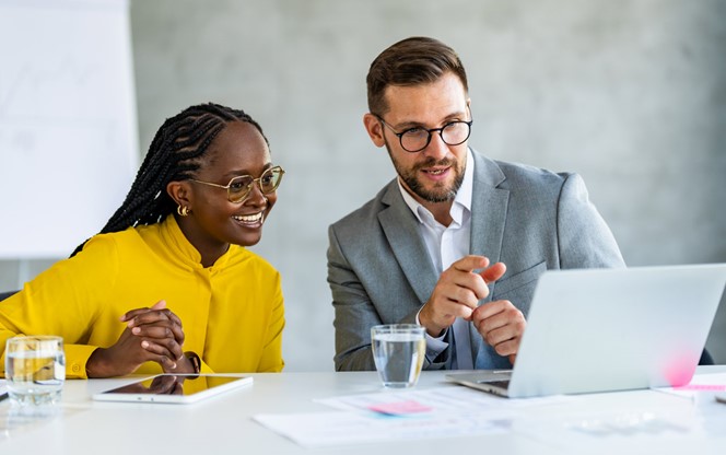 Two Business People Discussing Technology Looking At A Laptop In Office