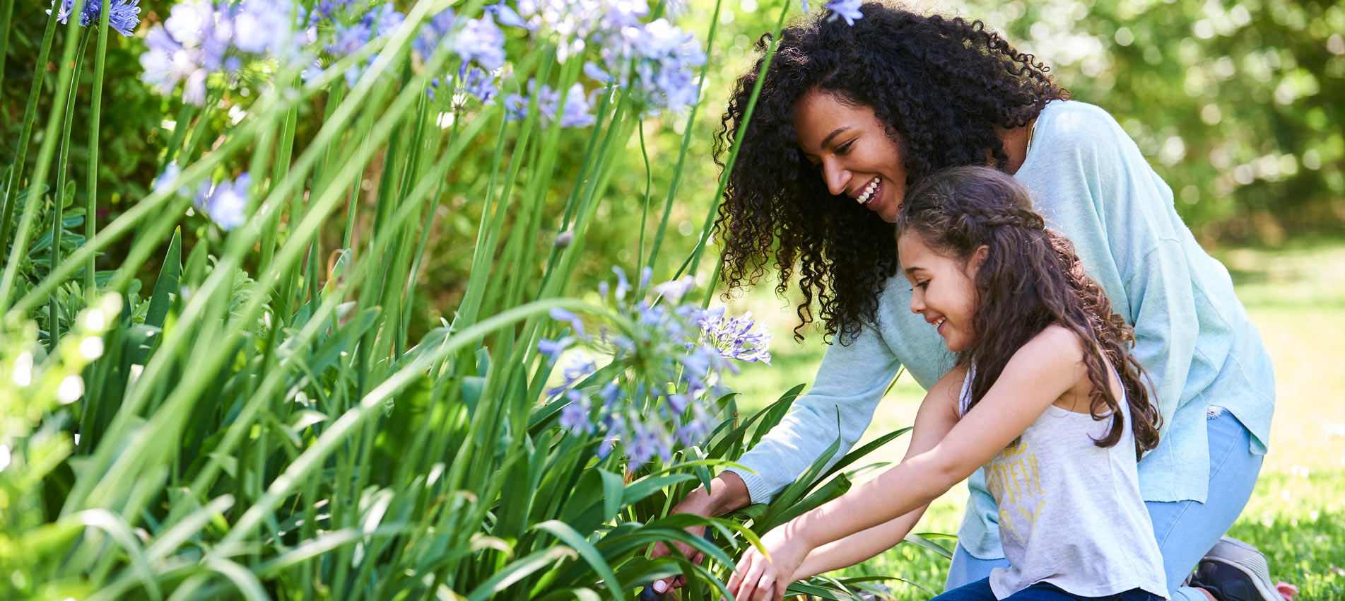 Mother And Daughter Planting Flowers In Garden